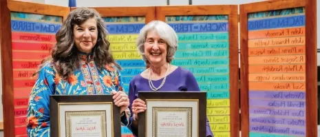 Two women holding up awards and smiling.